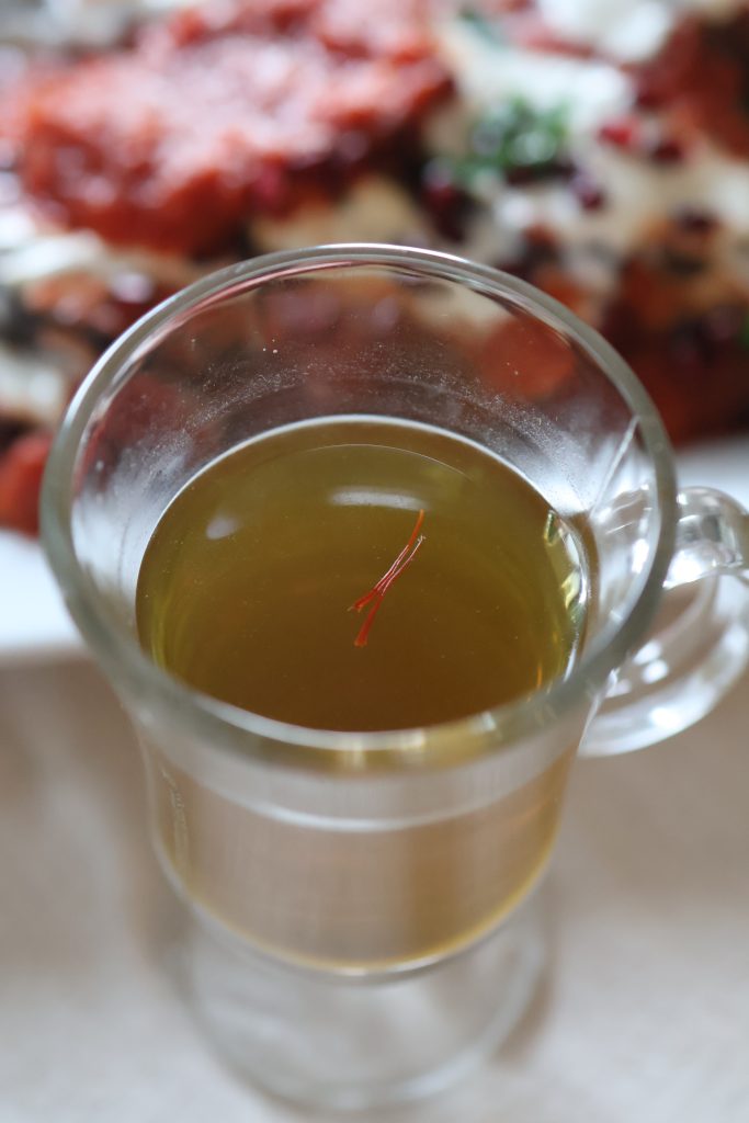 Cup of Afghan green tea infused with saffron, served alongside traditional Afghan dishes.