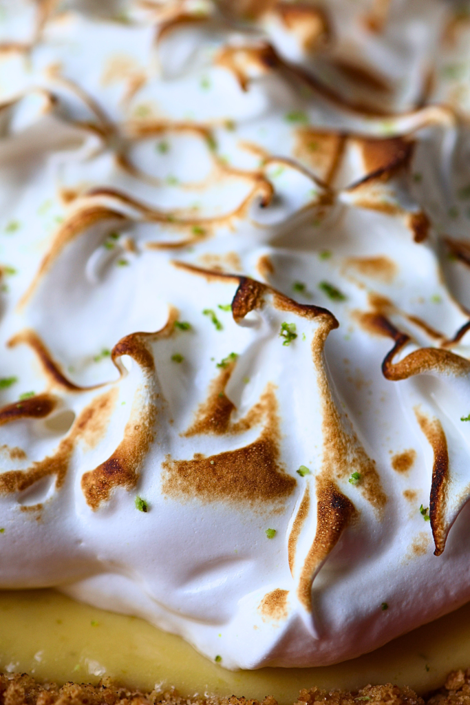 Macro close-up of toasted meringue peaks with golden-brown caramelized tips and lime zest on key lime pie