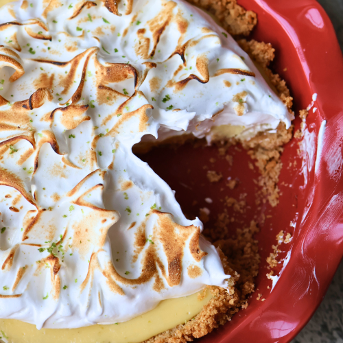 Sliced key lime pie with toasted meringue topping and graham cracker crust in a red ceramic pie dish