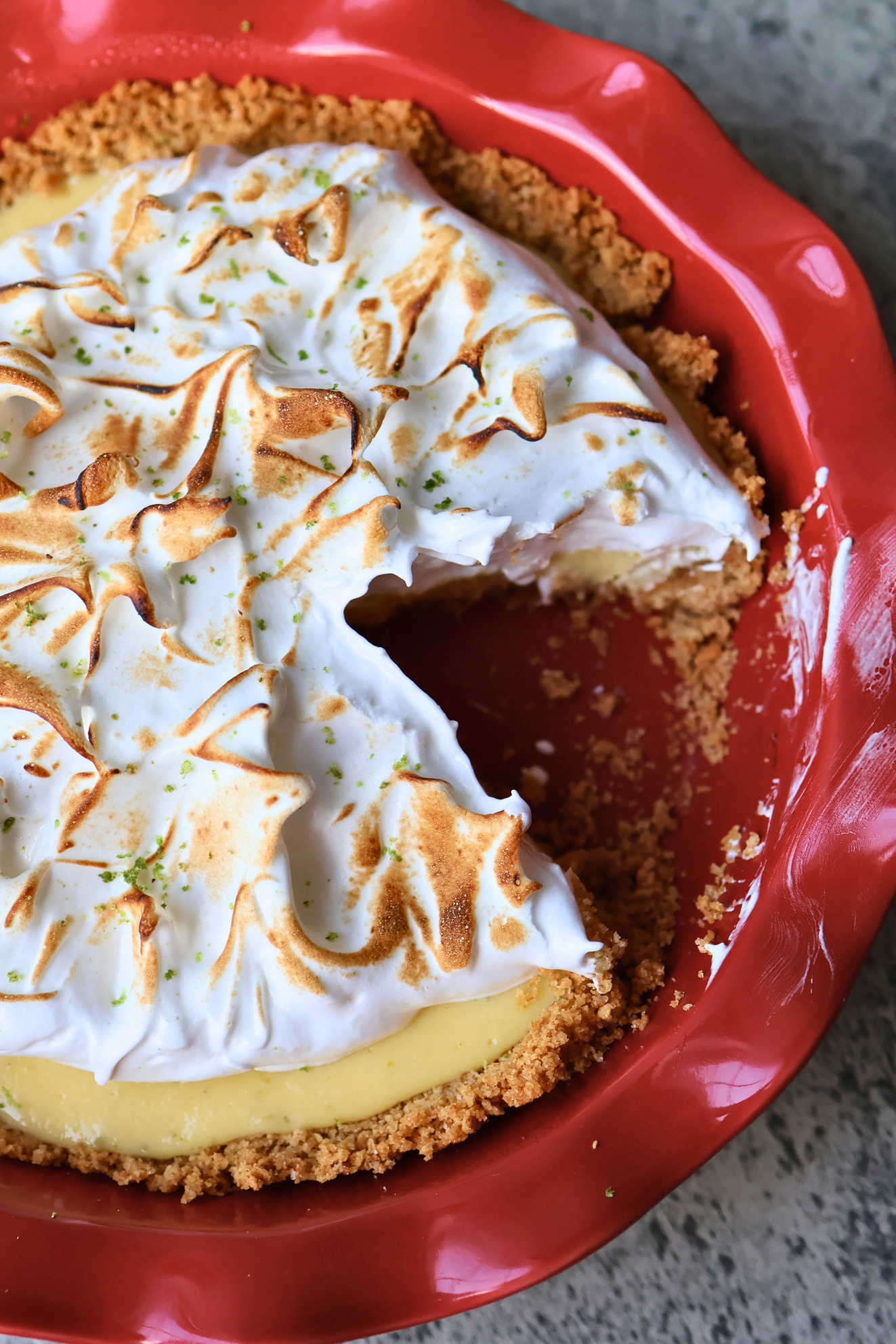 Sliced key lime pie with toasted meringue topping and graham cracker crust in a red ceramic pie dish
