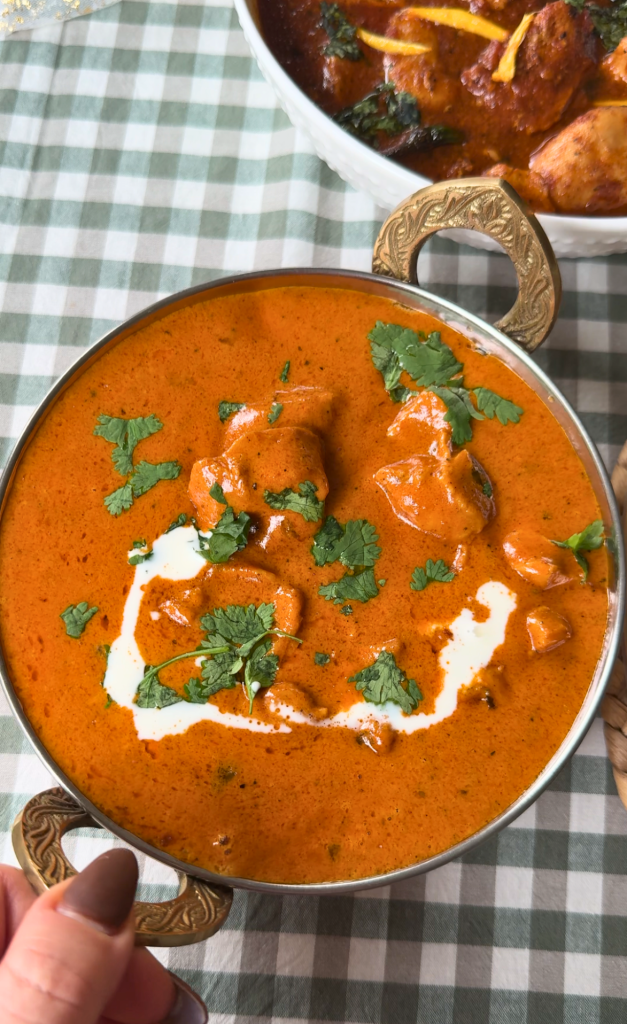 utter chicken served in a traditional copper bowl, garnished with cream and fresh cilantro.