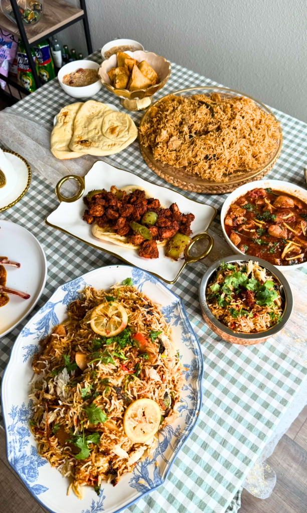 Pakistani feast featuring chicken pulao, butter chicken, lamb chops masala, chicken tikka boti, naan, and traditional side dishes arranged on a dining table.