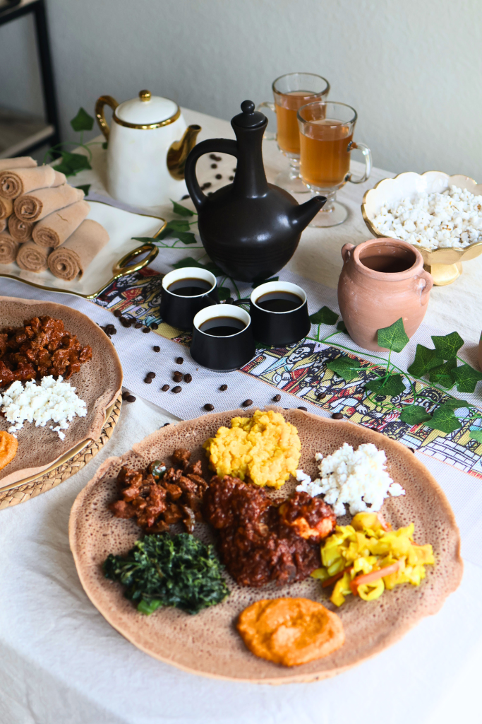 Traditional Ethiopian dining table featuring injera, doro wat, vegetables, popcorn, and a coffee ceremony setup with a jebena coffee pot.