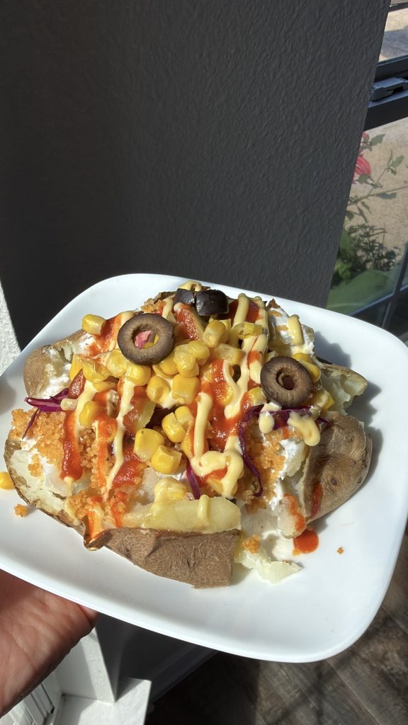 Turkish kumpir baked potato topped with corn, olives, red cabbage, and creamy sauces.
