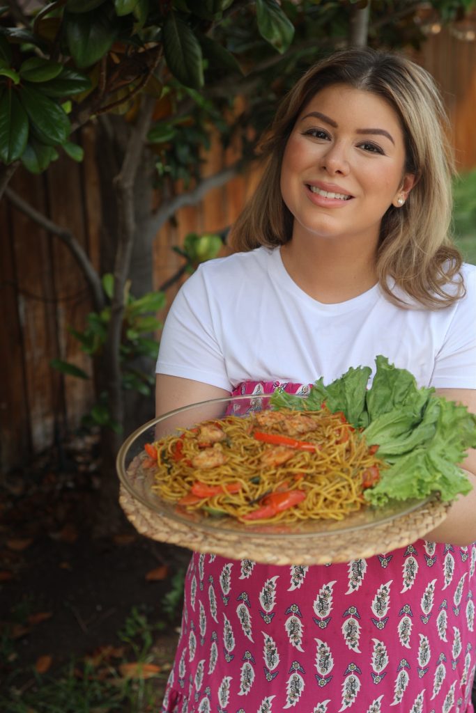 Emilia Kim holding a platter of traditional Malagasy mine sao, a stir-fried noodle dish with shrimp and vegetables, during her Hosting the World Madagascar dinner.