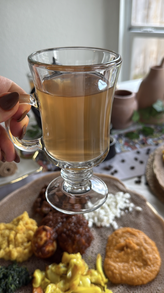 Cup of traditional Ethiopian tea served alongside an Ethiopian platter featuring doro wat, vegetables, and injera.