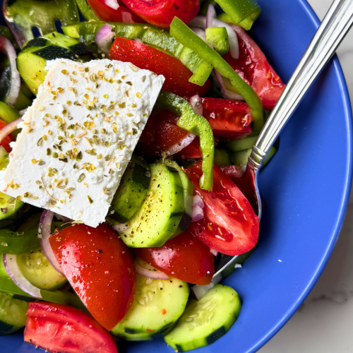 Traditional Greek horiatiki salad with tomatoes, cucumber, green bell pepper, red onion, Kalamata olives, and a block of feta cheese.
