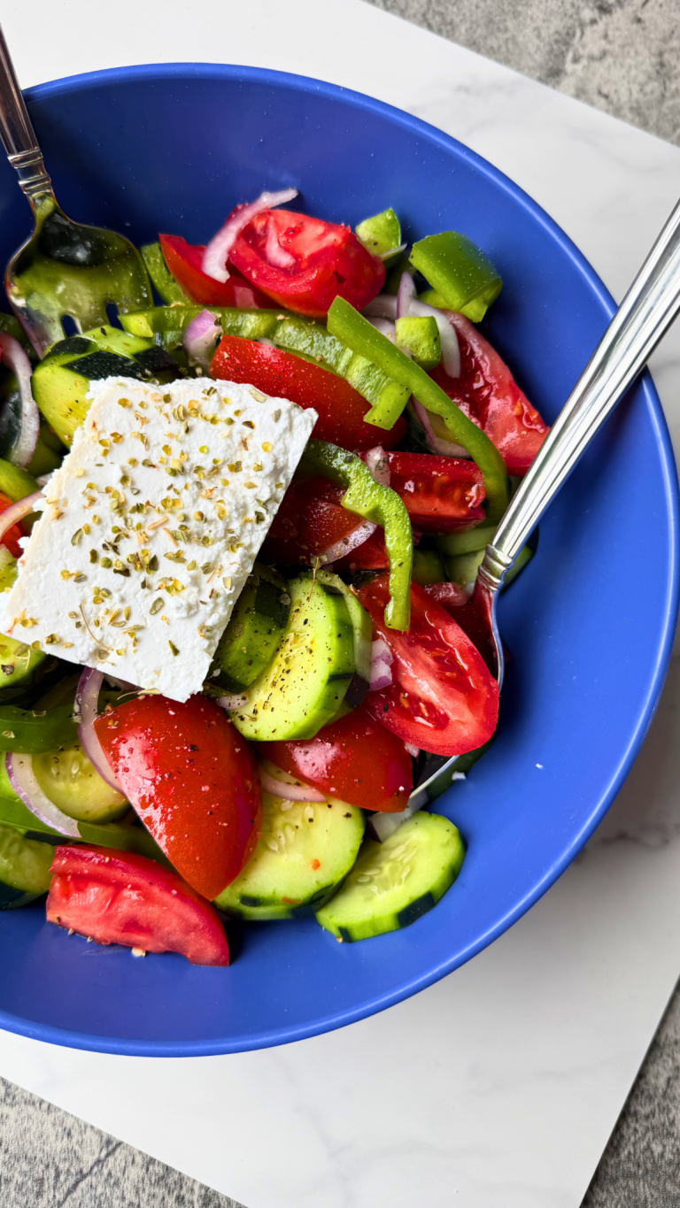 Traditional Greek horiatiki salad with tomatoes, cucumber, green bell pepper, red onion, Kalamata olives, and a block of feta cheese.