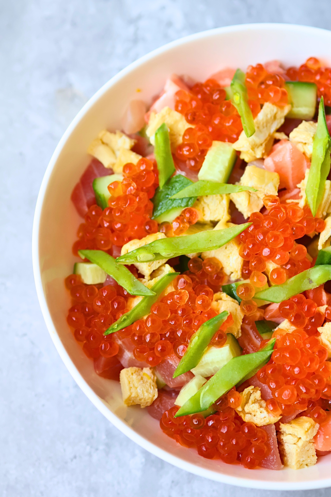 Traditional Japanese chirashizushi topped with salmon, ikura, avocado, cucumber, and sushi rice.