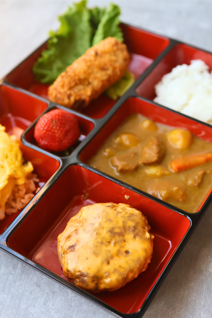 Traditional Japanese kids' meal with curry rice, hamburger steak, croquette, and vegetables served in a compartment tray.