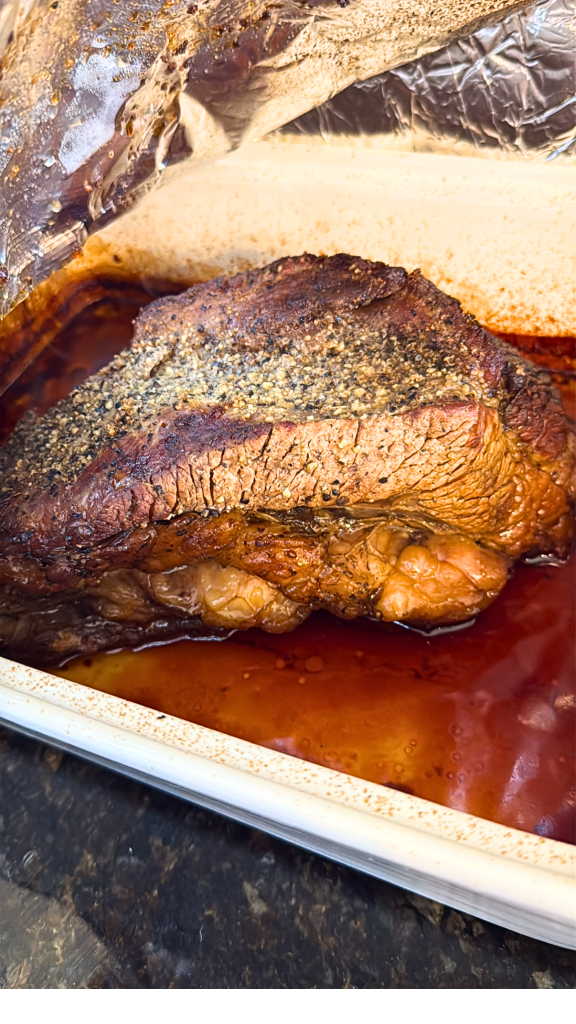 Smoked Texas beef brisket resting in its juices after a slow barbecue cook, featuring a dark bark and tender sliced meat.