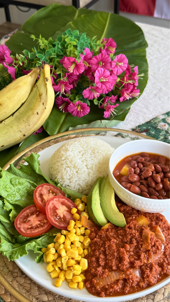 Traditional Puerto Rican corned beef served with white rice, stewed beans, avocado, sweet corn, lettuce, and fresh tomatoes on a dinner plate.