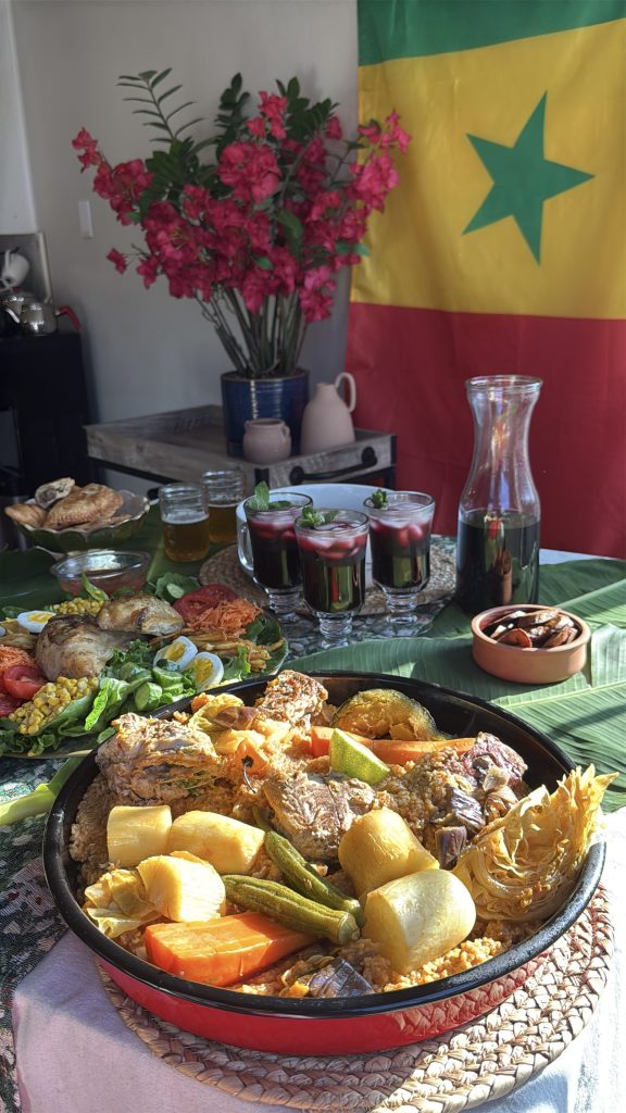 Traditional Senegalese dining table featuring thieboudienne, fresh salads, bissap, breads, and West African side dishes with a Senegal flag in the background.