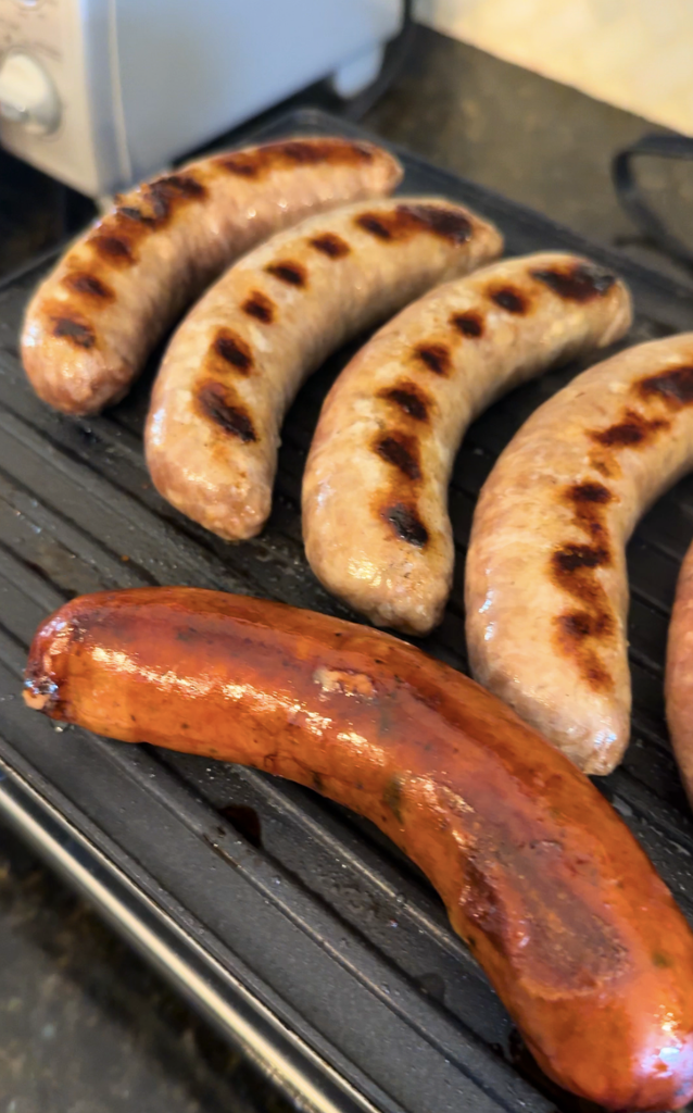 Grilled bratwurst sausages cooking over high heat, showcasing a classic American backyard barbecue favorite.