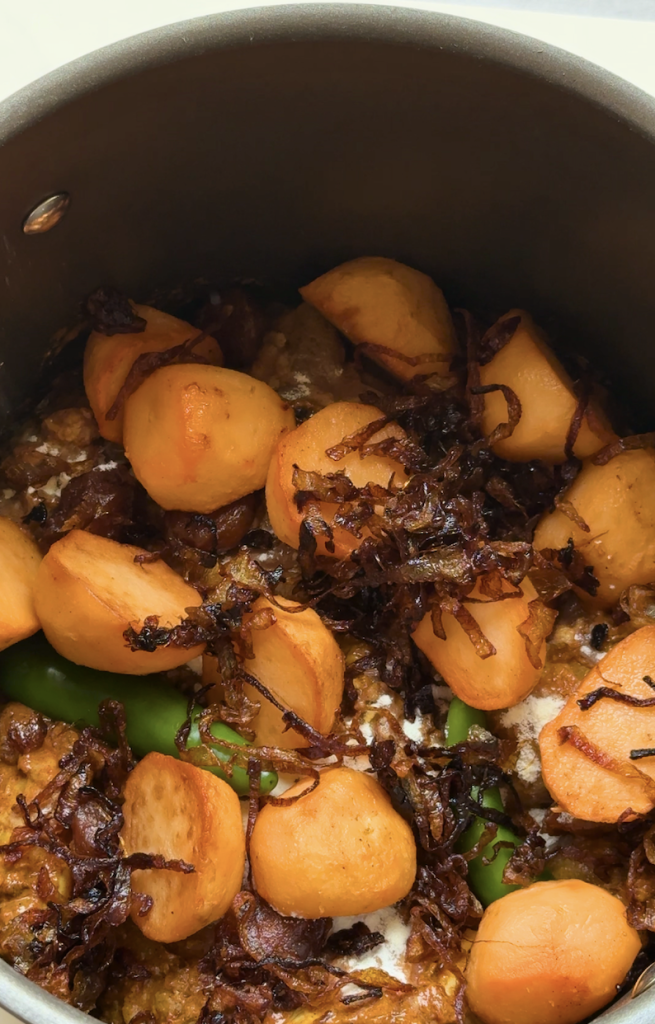 Close-up of an authentic Bangladeshi kacchi biryani being layered in a cooking pot with potatoes, crispy fried onions, whole green chilies, milk powder, and marinated mutton before slow dum cooking.