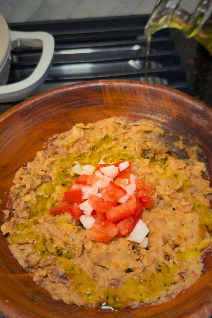 Traditional Egyptian ful medames topped with diced tomatoes, onions, and olive oil, served in a wooden bowl.