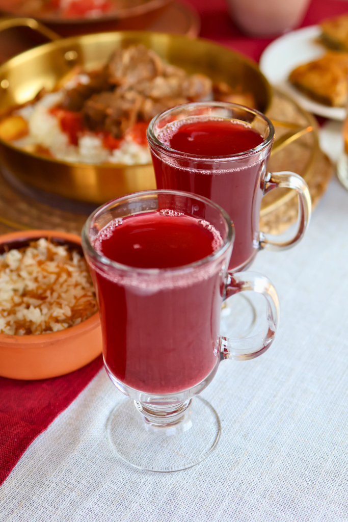 Two glass mugs of traditional Egyptian hibiscus tea (karkade) served hot on a table with Egyptian dishes in the background.