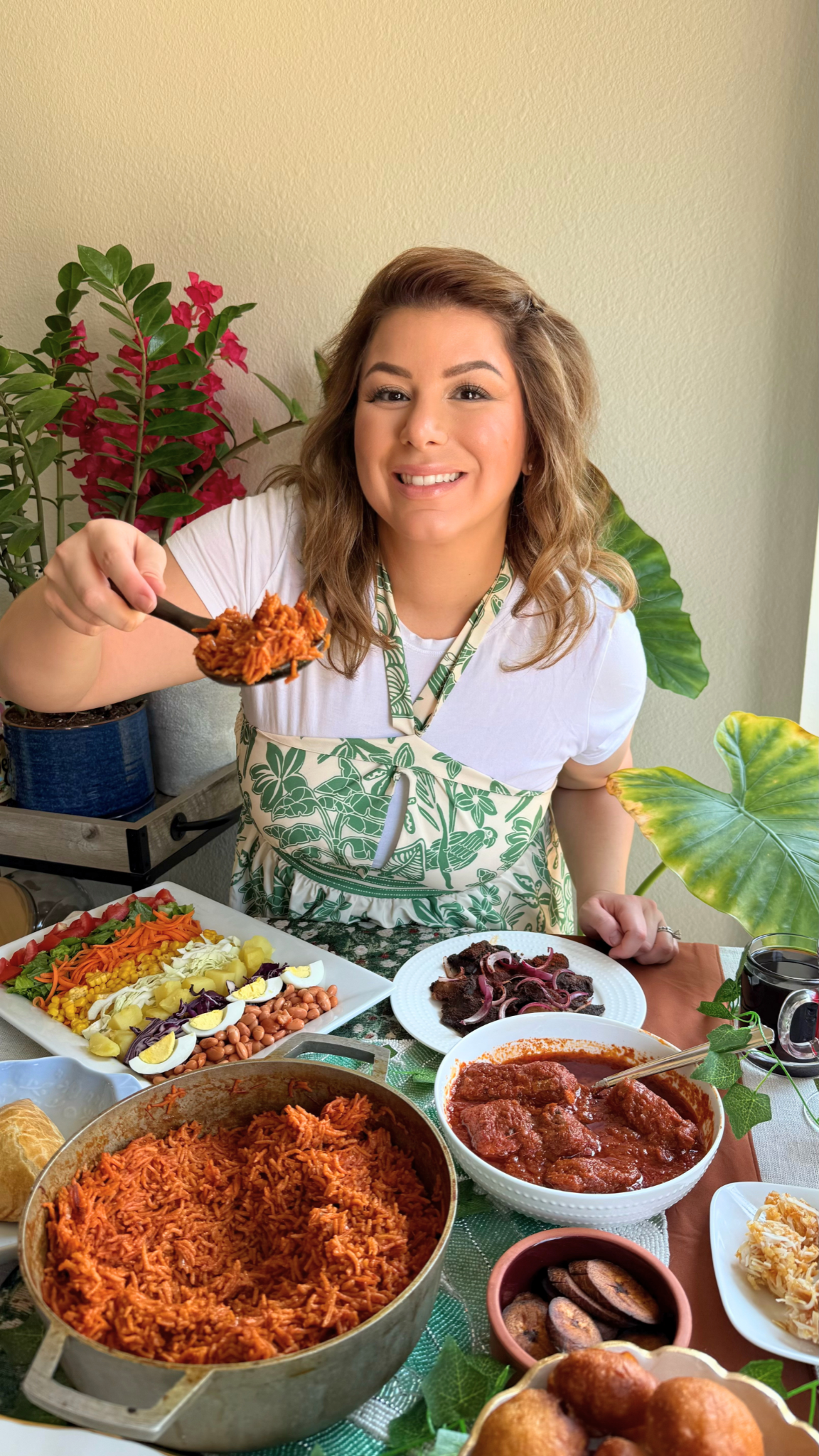 Emilia Kim presenting a traditional Nigerian meal featuring jollof rice, fish stew, beef suya, Nigerian salad, fried plantains, puff puff, and beef patties at a decorated dining table.