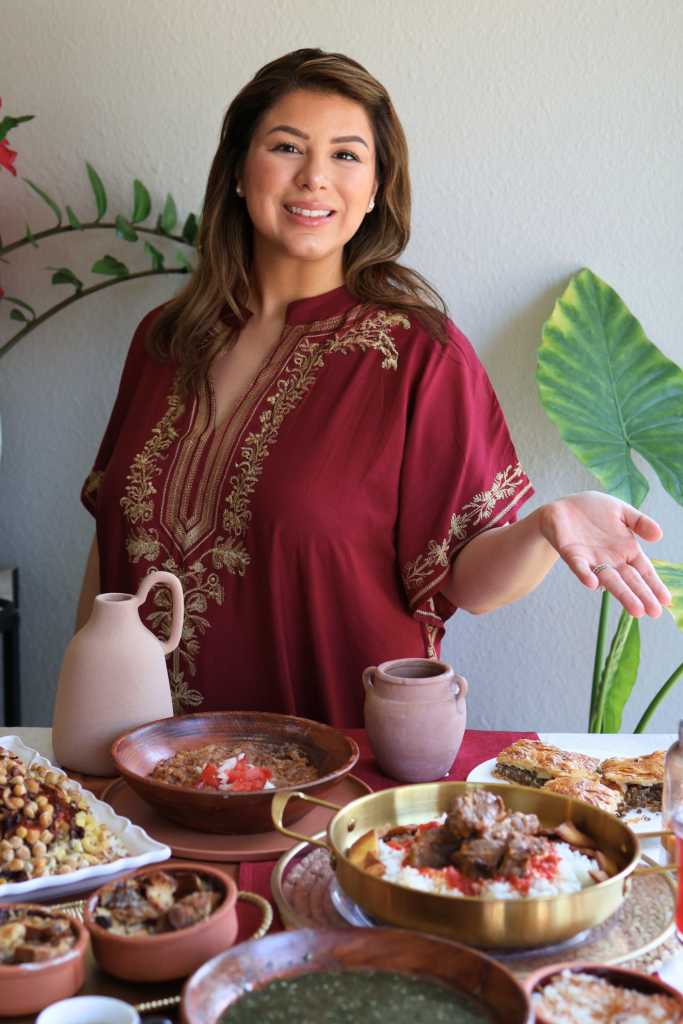 Emilia Kim standing beside a traditional Egyptian feast featuring koshari, fattah, molokhia, Egyptian goulash, Om Ali, and hibiscus tea.