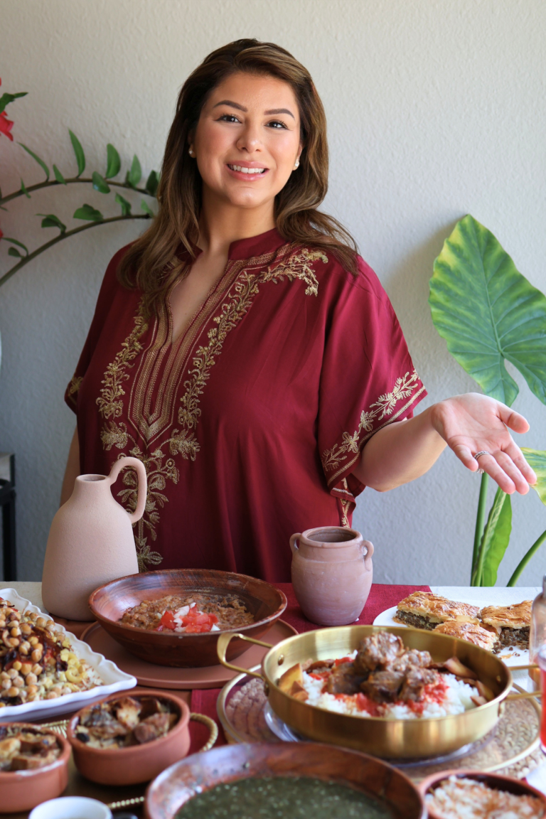 Emilia Kim standing beside a traditional Egyptian feast featuring koshari, fattah, molokhia, Egyptian goulash, Om Ali, and hibiscus tea.