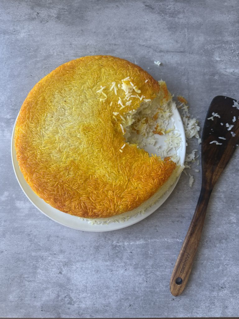 Golden Persian saffron tahdig with a crispy rice crust, flipped onto a plate and partially served to reveal fluffy basmati rice inside.