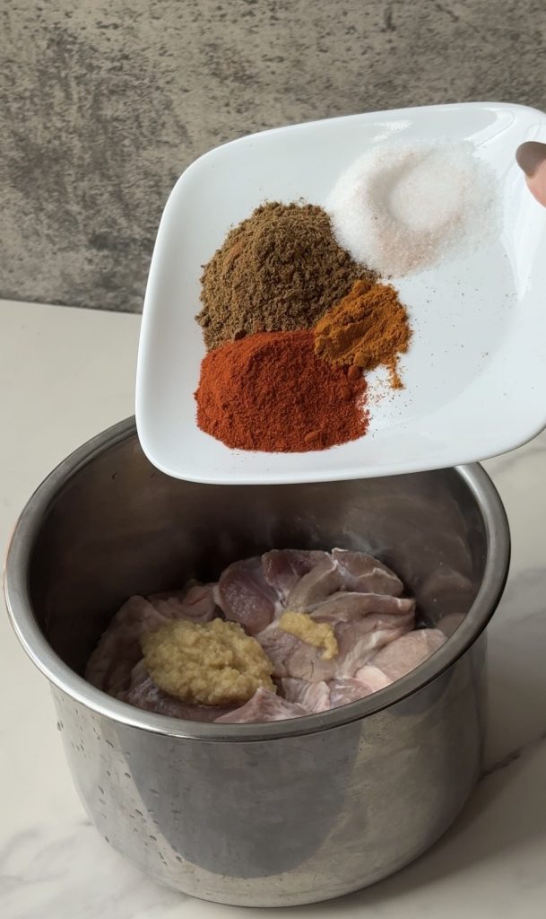 Ground spices being added to raw chicken in a mixing bowl to marinate for traditional Bangladeshi kacchi biryani.