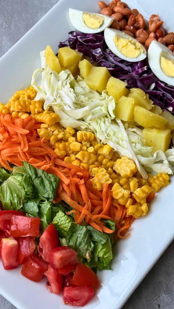 Traditional Nigerian salad arranged with lettuce, tomatoes, carrots, cabbage, sweet corn, potatoes, baked beans, and hard-boiled eggs on a white serving platter.