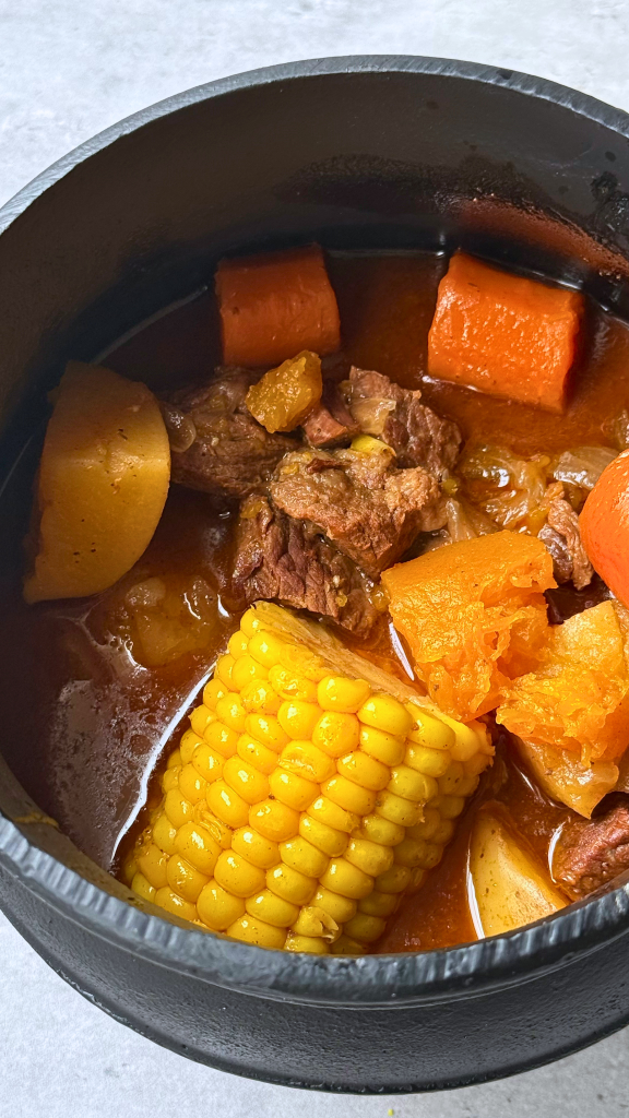 South African potjiekos stew with beef, potatoes, carrots, sweet potato, and corn cooked in a traditional potjie pot