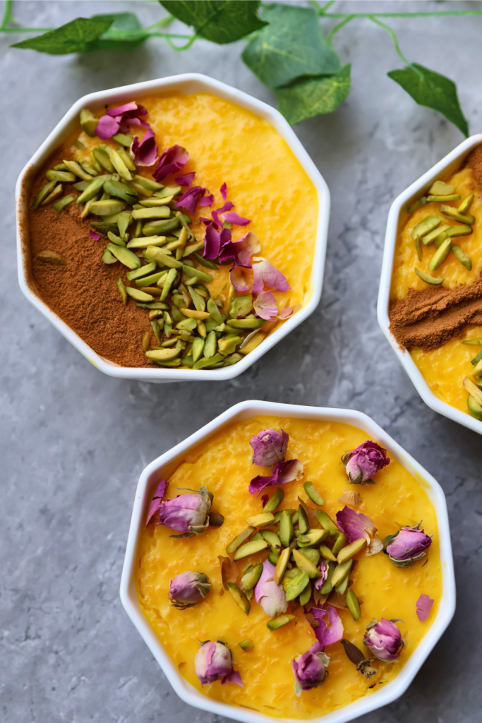 Bowls of traditional Persian sholeh zard saffron rice pudding garnished with pistachios, cinnamon, and dried rose petals.