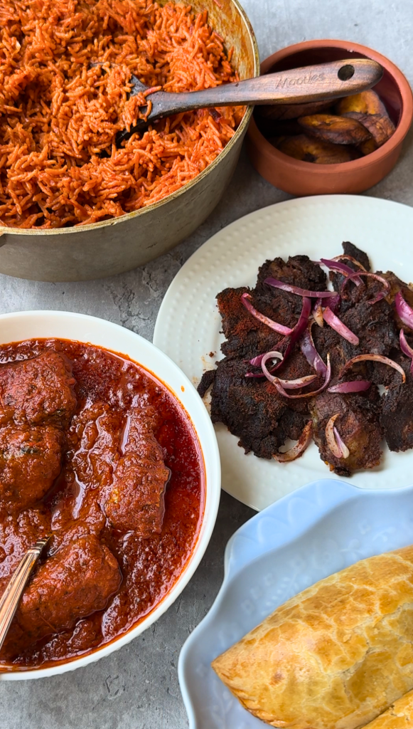 Traditional Nigerian meal featuring jollof rice, beef suya, fish stew, fried plantains, and Nigerian beef patties served on a table.