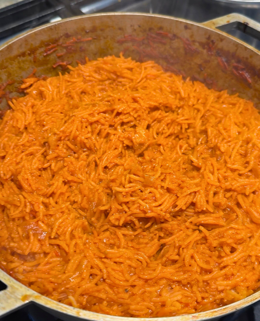 Homemade Nigerian jollof rice cooking in a large pot with long-grain basmati rice coated in a rich tomato and pepper sauce.