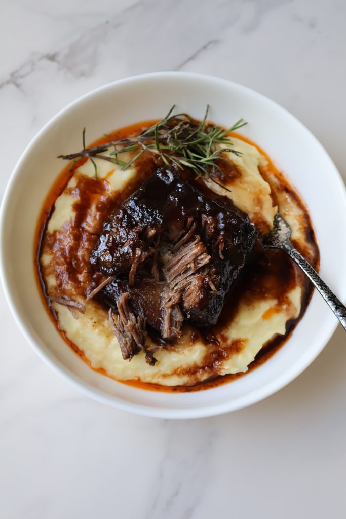Maple and red wine braised short ribs served over mashed potatoes, topped with rosemary sprigs and glossy sauce.